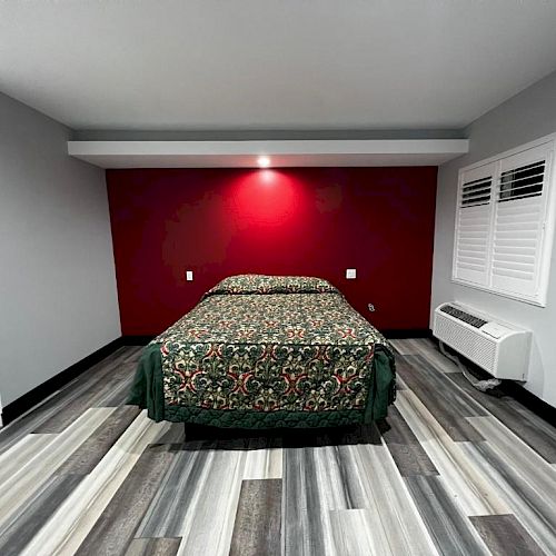 The image shows a modern bedroom with a bed centered against a red accent wall, wood-pattern flooring, and minimalistic decor, ending the sentence.