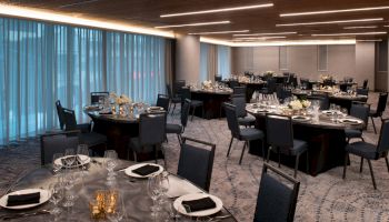 The image shows an elegantly set dining room with round tables adorned with black tablecloths, flower centerpieces, and set with glassware and silverware.