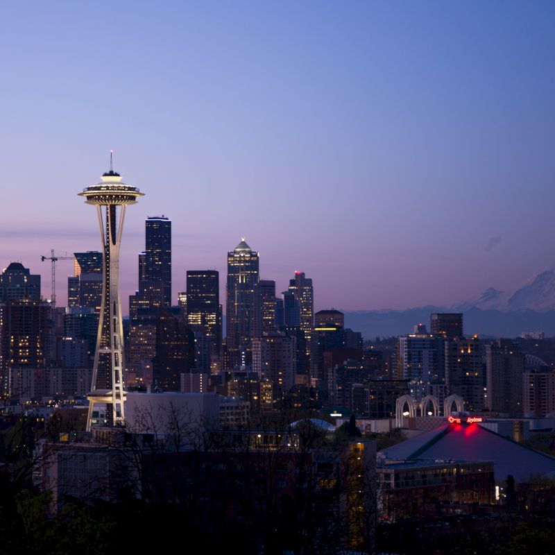 This image shows a cityscape featuring the Space Needle, surrounded by skyscrapers, with a mountain in the background, captured at twilight.
