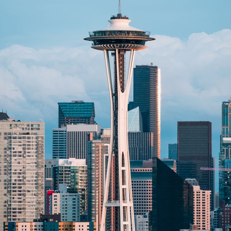 The image features a skyline with the Space Needle prominently in the foreground, set against other skyscrapers and a backdrop of cloudy skies.