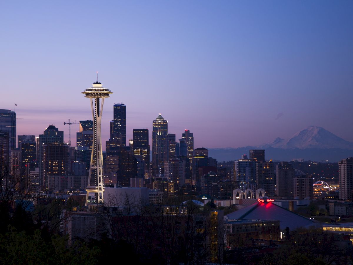 The image shows the Seattle skyline at dusk, with the Space Needle prominently displayed and Mount Rainier visible in the background.