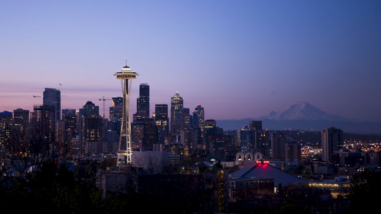 The image shows the Seattle skyline at dusk, with the Space Needle prominently displayed and Mount Rainier visible in the background.